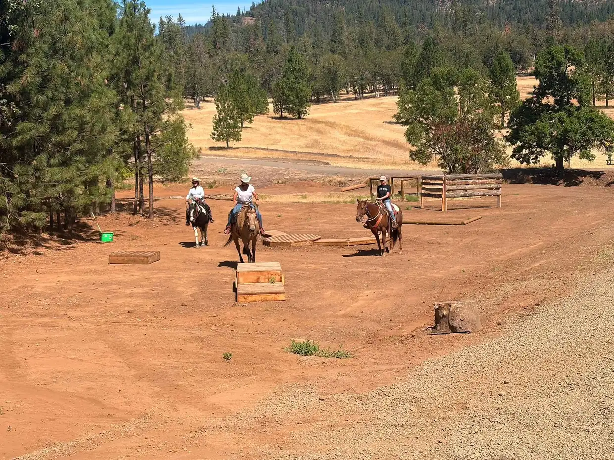 Three riders on the open arena ground among bridges and podiums, hills behind